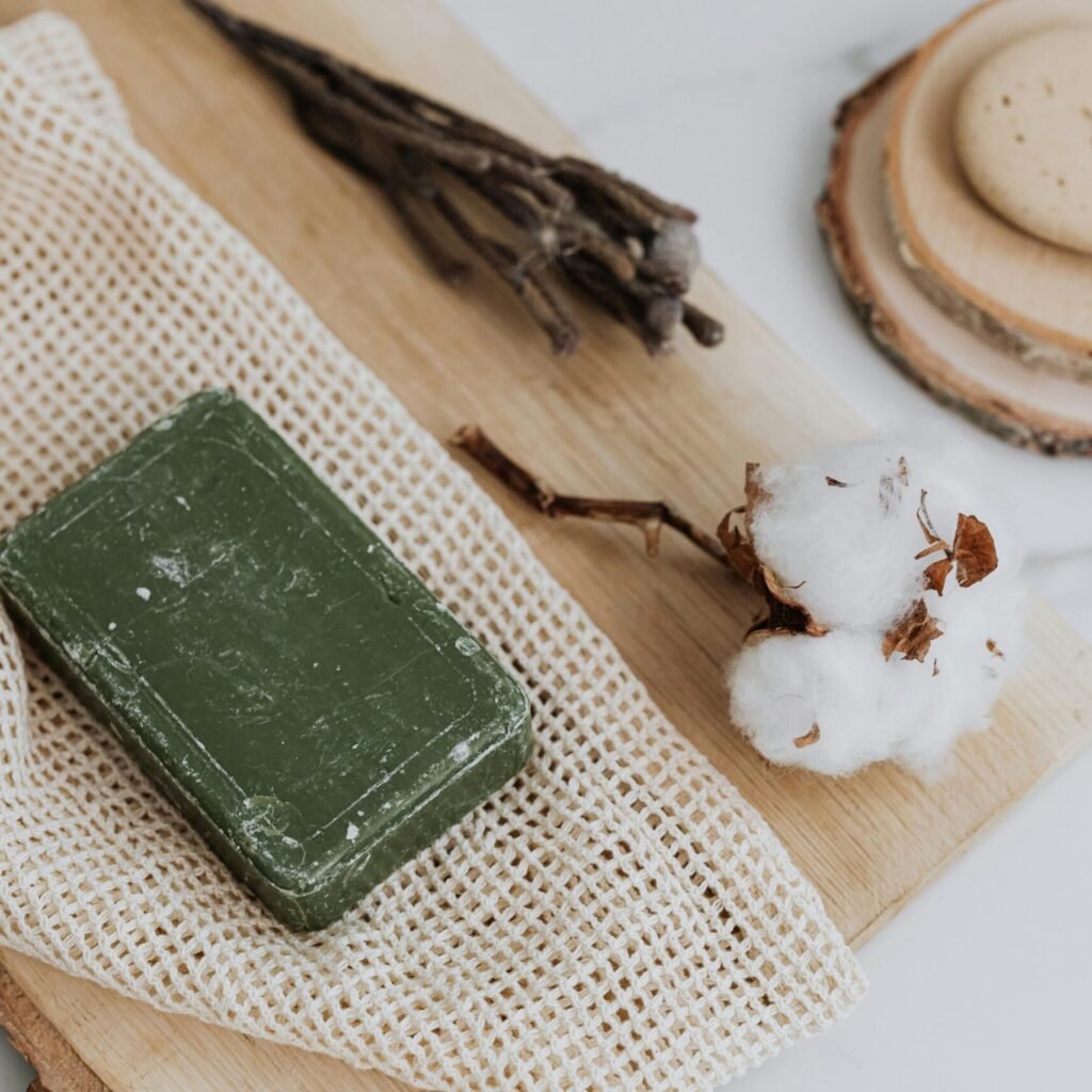 Natural green soap with cotton and loofah on wooden board promoting zero waste lifestyle.